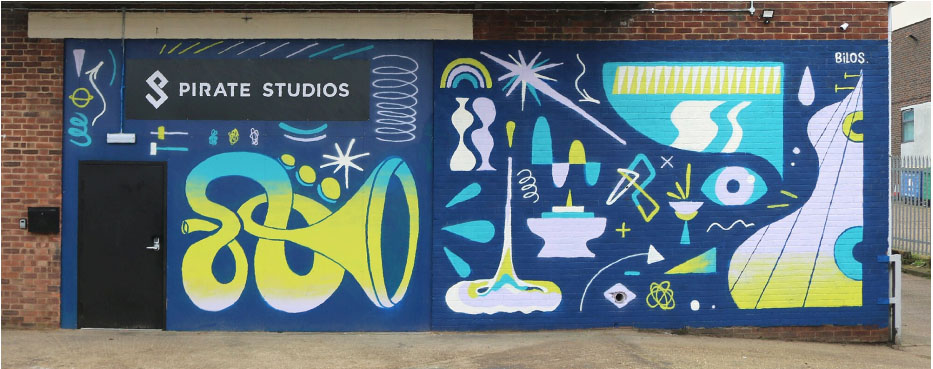  graffiti in blue and yellow over the brick and a black security door with black sign above it saying pirate studios in white